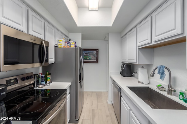 kitchen featuring sink, light hardwood / wood-style flooring, a tray ceiling, stainless steel appliances, and white cabinets