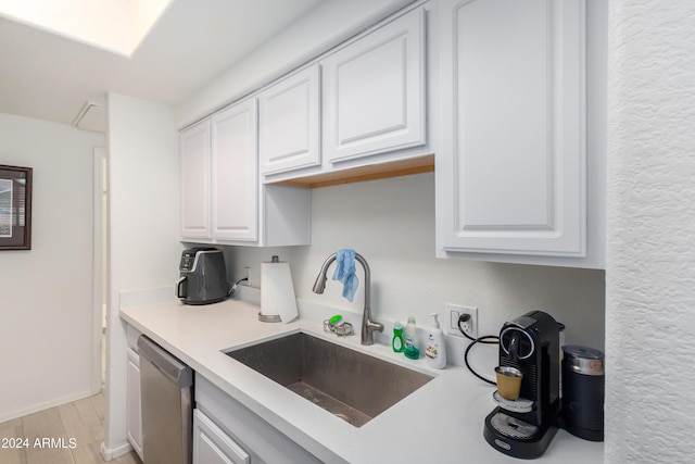 kitchen featuring white cabinetry, sink, stainless steel dishwasher, and light hardwood / wood-style floors