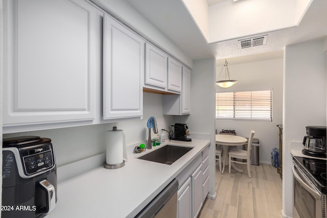 kitchen featuring sink, pendant lighting, stainless steel appliances, light hardwood / wood-style floors, and white cabinets