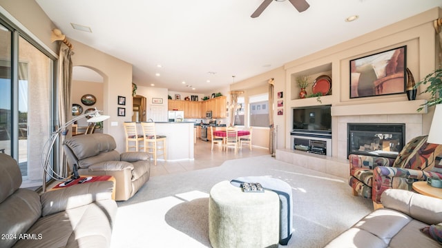 living room featuring a tiled fireplace, ceiling fan, a healthy amount of sunlight, and light tile patterned flooring