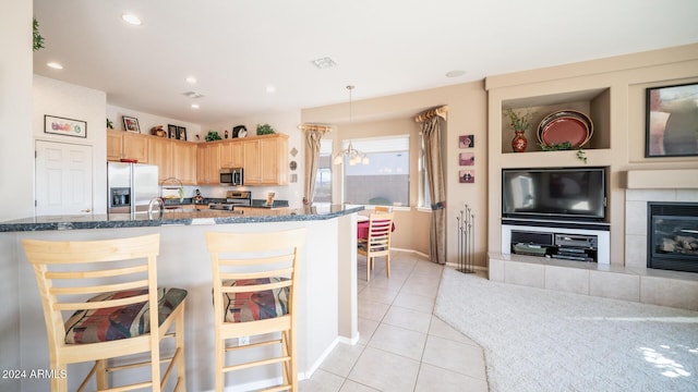 kitchen with light brown cabinets, a tile fireplace, hanging light fixtures, appliances with stainless steel finishes, and a kitchen bar