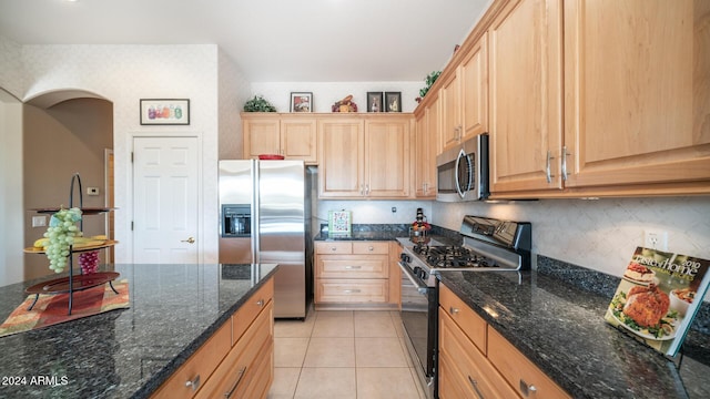 kitchen featuring light brown cabinets, backsplash, dark stone counters, light tile patterned floors, and appliances with stainless steel finishes