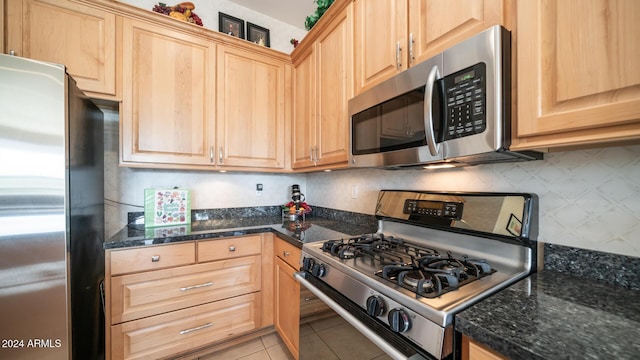 kitchen featuring light brown cabinets, stainless steel appliances, dark stone countertops, and light tile patterned flooring