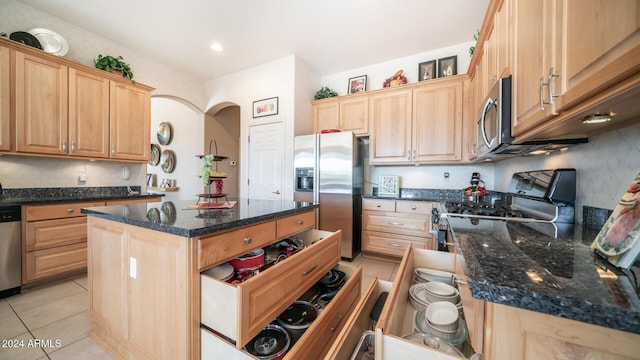 kitchen with light tile patterned floors, a center island, stainless steel appliances, and dark stone counters