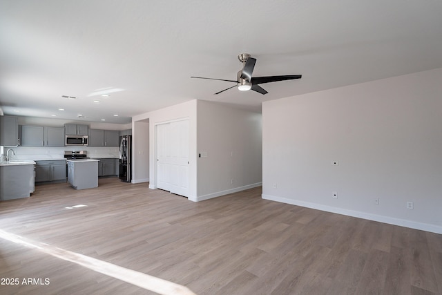 unfurnished living room with light wood-type flooring, sink, and ceiling fan