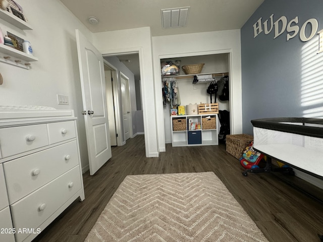 bedroom with dark wood-style floors, visible vents, baseboards, and a closet