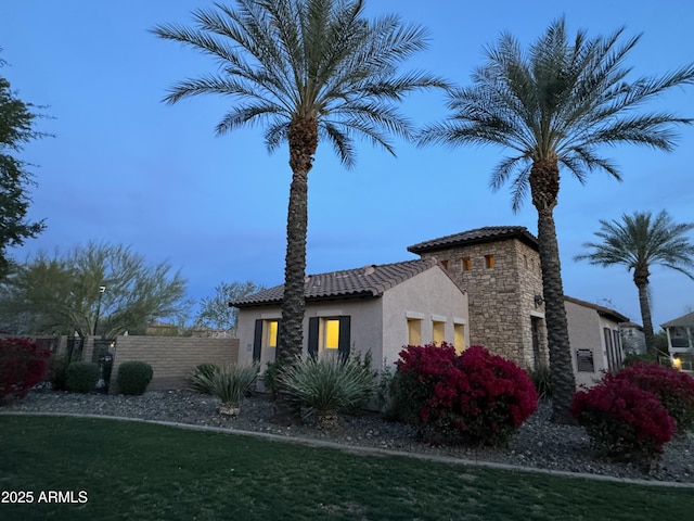 view of side of property with stucco siding, stone siding, fence, and a tiled roof