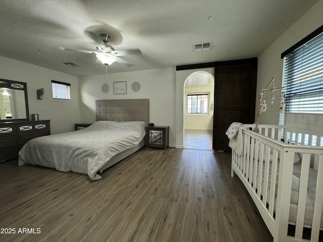 bedroom with a textured ceiling, wood finished floors, visible vents, and arched walkways