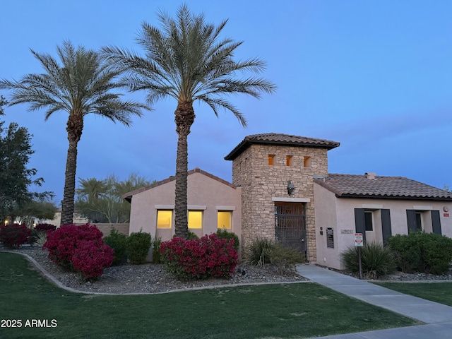 mediterranean / spanish-style home with stucco siding, stone siding, a front yard, and a tile roof