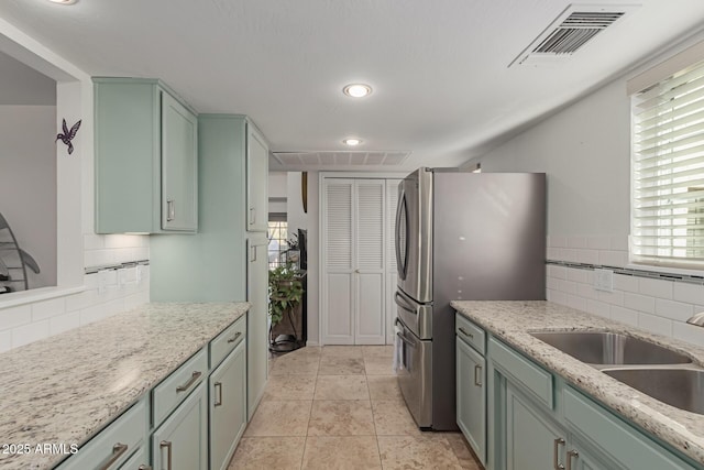 kitchen featuring visible vents, freestanding refrigerator, light stone countertops, green cabinets, and a sink