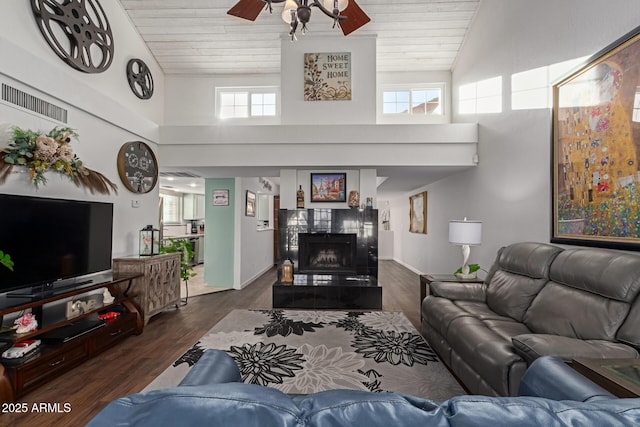 living room with dark wood-style floors, a fireplace, visible vents, ceiling fan, and wooden ceiling