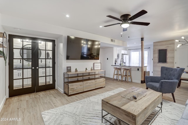 living room with french doors, sink, light hardwood / wood-style flooring, and ceiling fan with notable chandelier