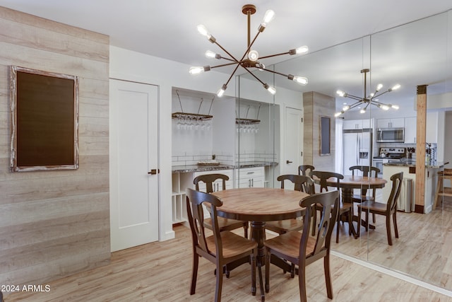 dining area with light hardwood / wood-style floors, an inviting chandelier, and wood walls