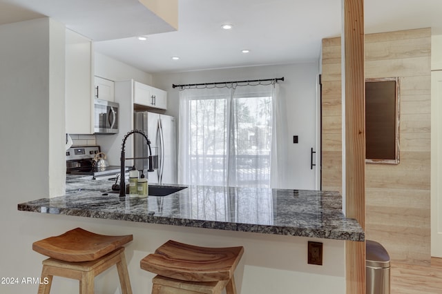 kitchen featuring a breakfast bar area, white cabinetry, light wood-type flooring, dark stone countertops, and stainless steel appliances