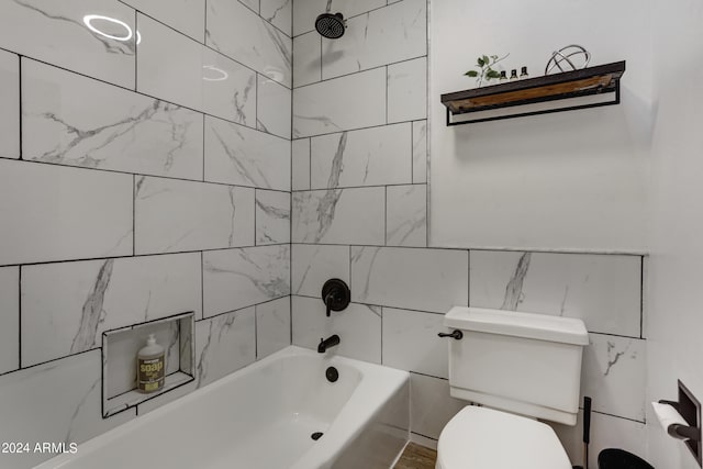 bathroom with tile walls, tiled shower / bath combo, and toilet