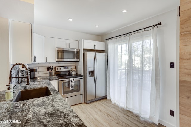 kitchen with sink, stone counters, appliances with stainless steel finishes, light hardwood / wood-style floors, and tasteful backsplash