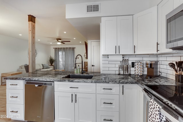 kitchen with appliances with stainless steel finishes, sink, white cabinetry, dark stone counters, and decorative backsplash