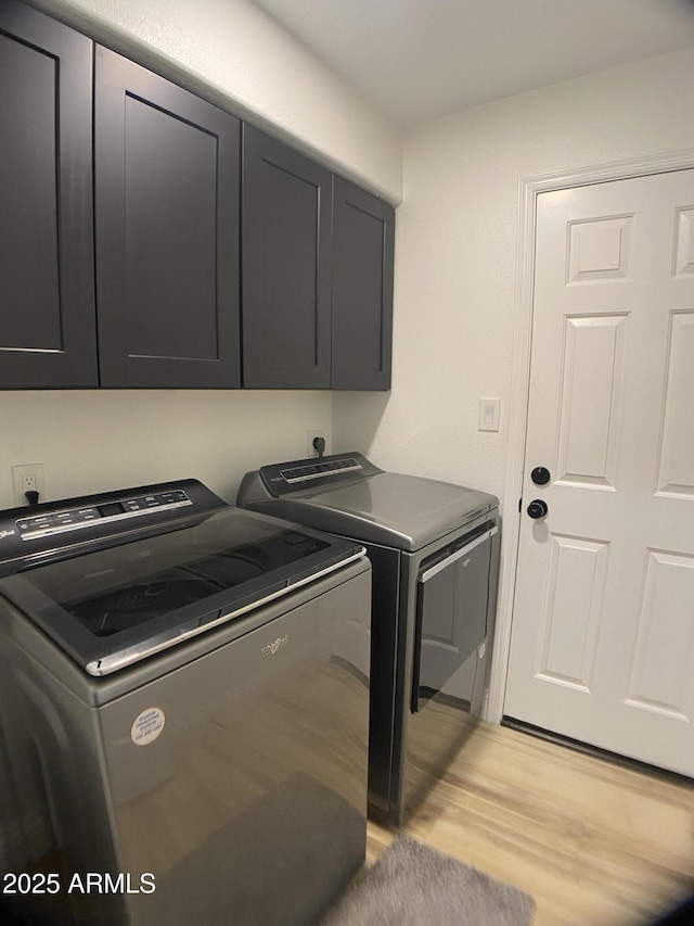 laundry room featuring cabinets, light wood-type flooring, and washing machine and clothes dryer