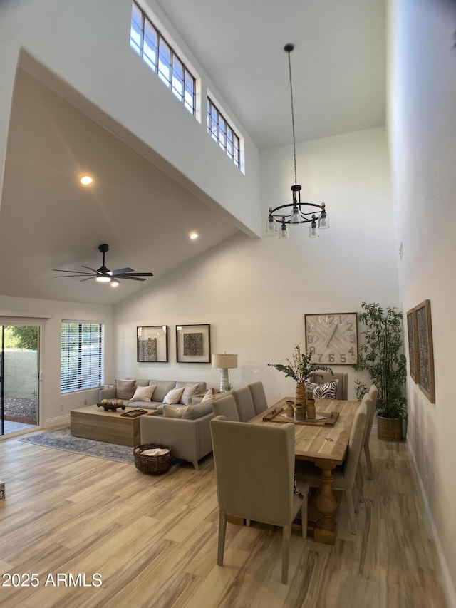 dining room featuring ceiling fan with notable chandelier, a high ceiling, and light hardwood / wood-style flooring