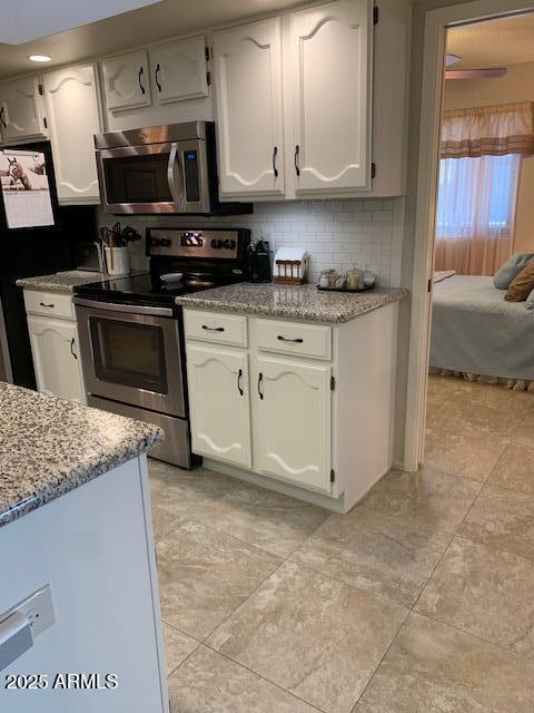 kitchen with light stone counters, stainless steel appliances, backsplash, and white cabinets