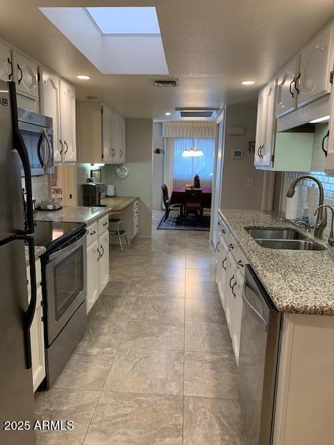 kitchen featuring sink, a skylight, stainless steel appliances, light stone countertops, and white cabinets