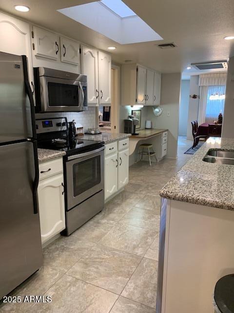 kitchen with white cabinetry, a skylight, appliances with stainless steel finishes, light stone countertops, and decorative backsplash