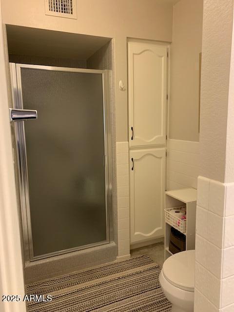 bathroom featuring tile patterned floors, toilet, and a shower with shower door