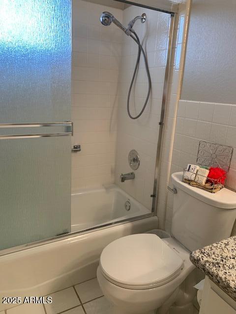 full bathroom featuring shower / bath combination with glass door, tile patterned flooring, tile walls, vanity, and toilet