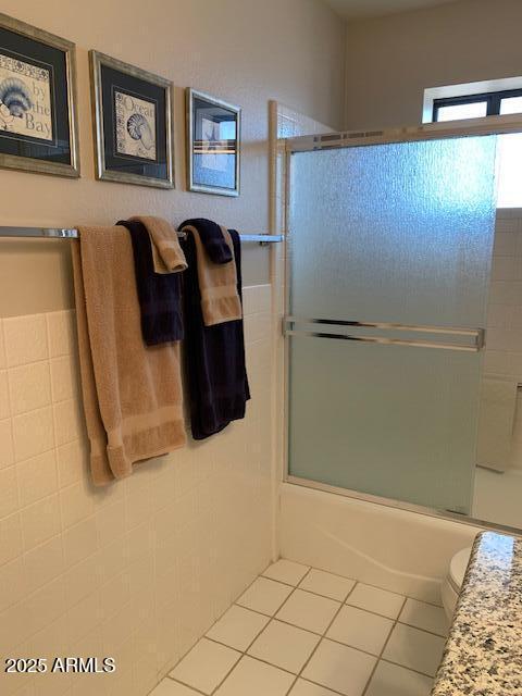 bathroom featuring toilet, tile patterned flooring, and combined bath / shower with glass door