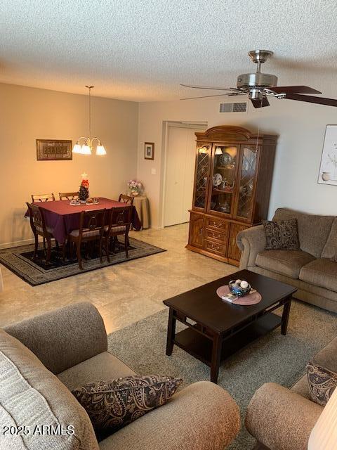 living room featuring ceiling fan with notable chandelier and a textured ceiling