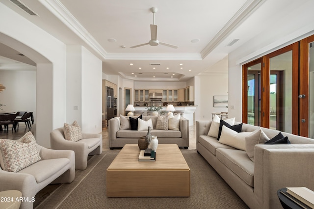 living room with a raised ceiling, ornamental molding, and ceiling fan