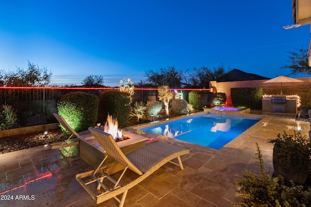 pool at dusk with a patio area, exterior kitchen, and an outdoor fire pit