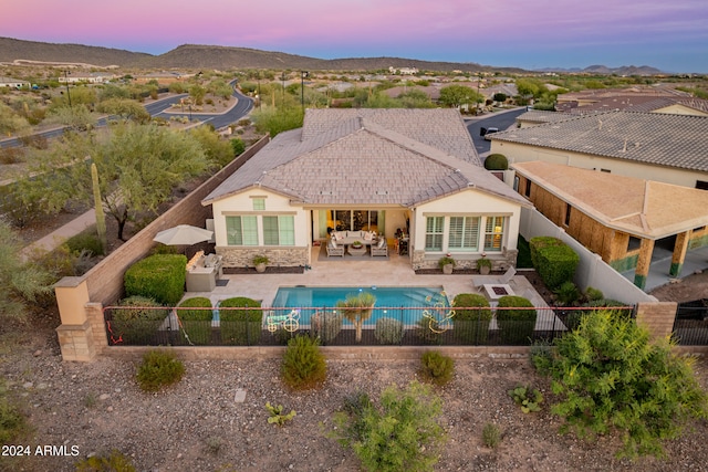 back house at dusk with a fenced in pool, outdoor lounge area, a patio area, and a mountain view