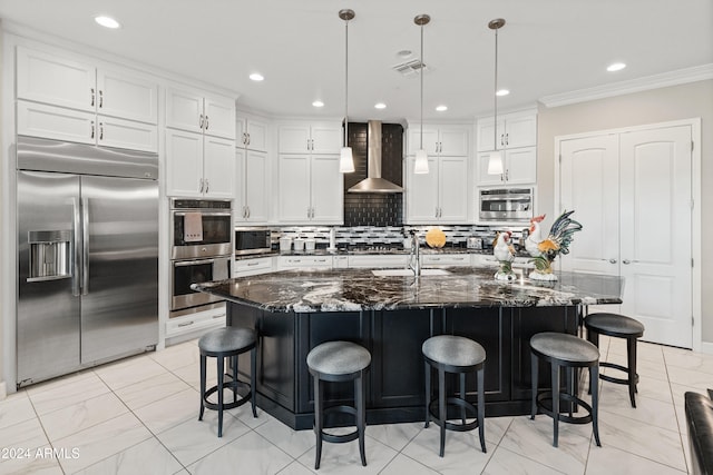 kitchen with stainless steel appliances, a center island with sink, dark stone countertops, and wall chimney range hood