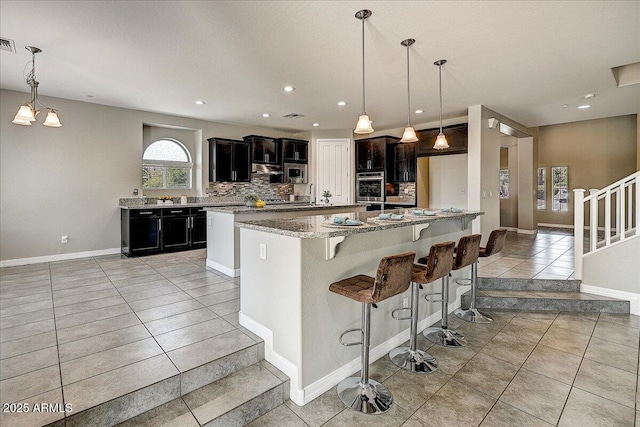 18207 W Sells Dr, Goodyear, AZ 85395 - kitchen featuring light tile patterned floors, tasteful backsplash, a kitchen island, a kitchen bar, and stainless steel appliances