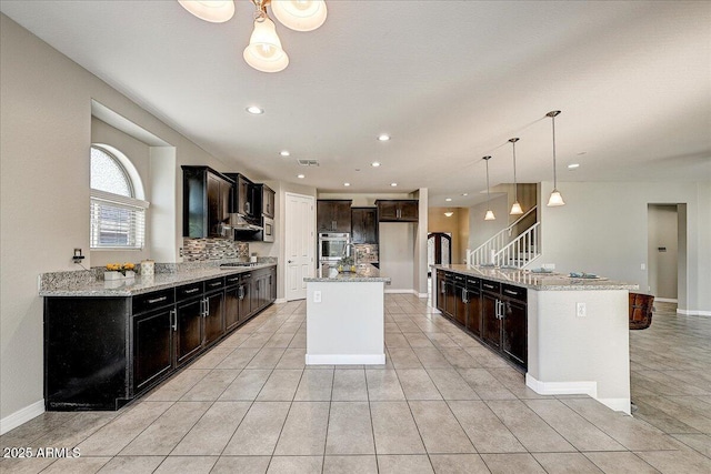 18207 W Sells Dr, Goodyear, AZ 85395 - kitchen with an island with sink, light tile patterned floors, light stone counters, hanging light fixtures, and recessed lighting