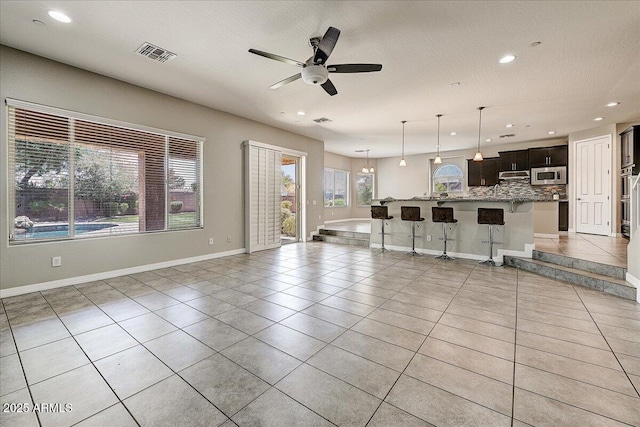 18207 W Sells Dr, Goodyear, AZ 85395 - kitchen featuring stainless steel microwave, light tile patterned floors, open floor plan, backsplash, and a breakfast bar area