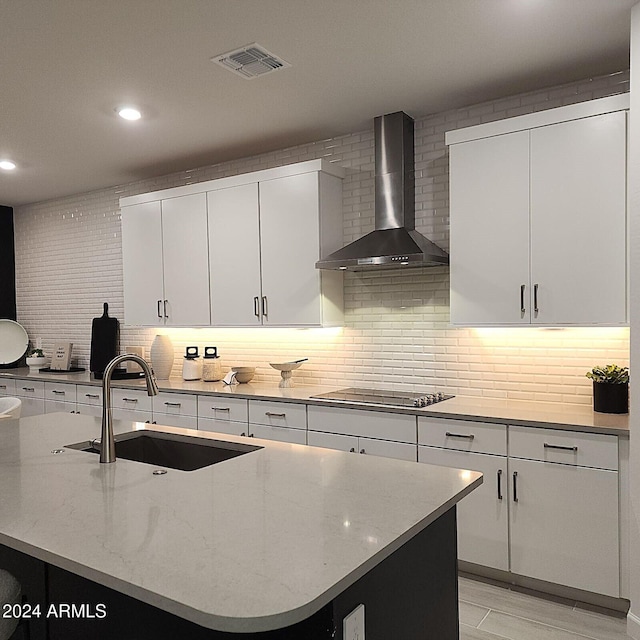 kitchen with sink, white cabinetry, a center island with sink, black electric cooktop, and wall chimney range hood