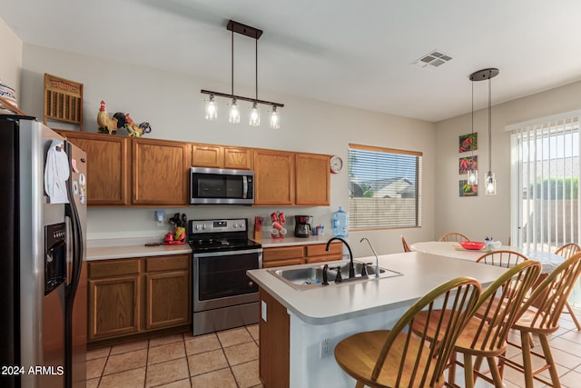 kitchen featuring appliances with stainless steel finishes, sink, an island with sink, hanging light fixtures, and a breakfast bar area