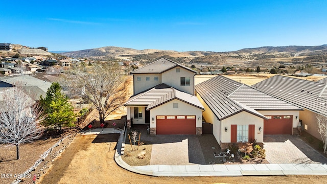 view of front of house with an attached garage, a mountain view, stone siding, decorative driveway, and stucco siding