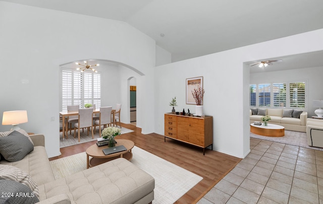 living room featuring ceiling fan with notable chandelier, light wood-type flooring, and vaulted ceiling