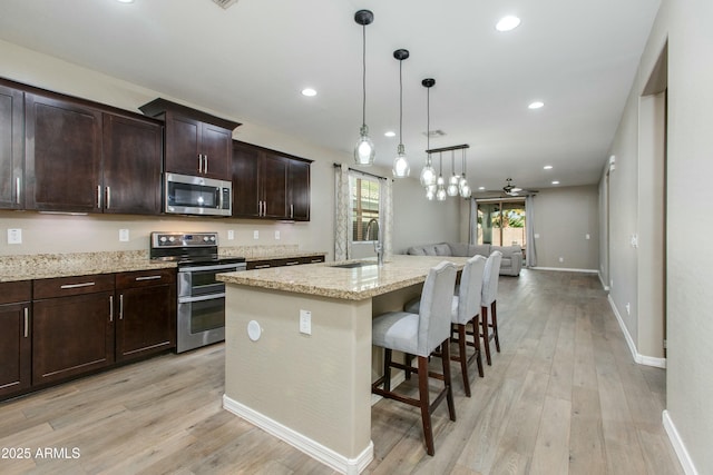 kitchen with dark brown cabinetry, a breakfast bar area, a kitchen island with sink, stainless steel appliances, and a sink