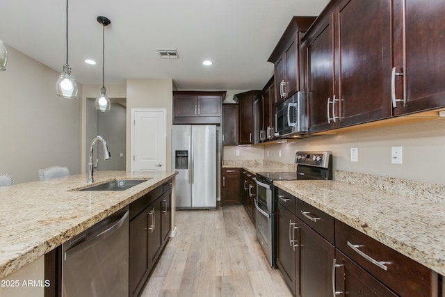 kitchen with light stone counters, stainless steel appliances, a sink, visible vents, and hanging light fixtures