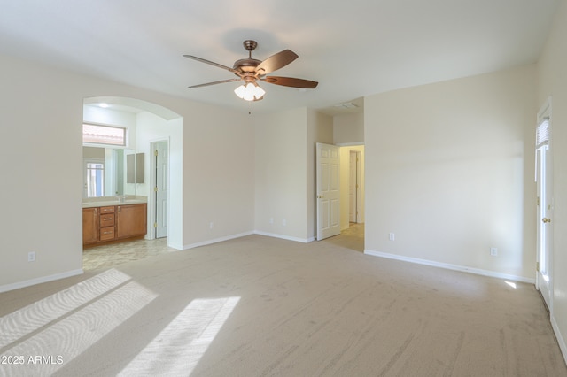 unfurnished bedroom featuring light carpet, ceiling fan, multiple windows, and ensuite bath