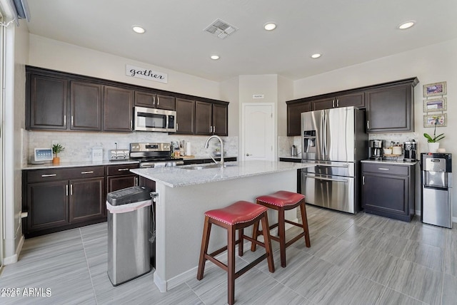 kitchen featuring a kitchen breakfast bar, stainless steel appliances, an island with sink, light stone countertops, and sink