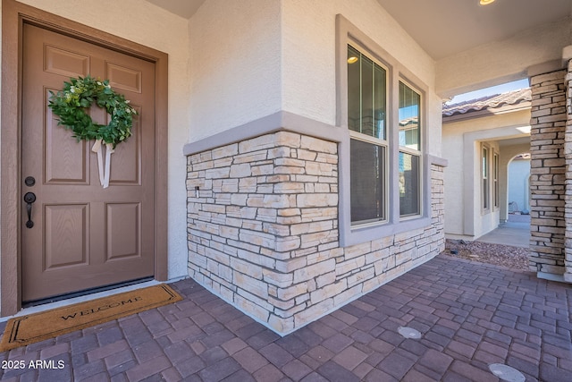 entrance to property featuring stone siding, a tiled roof, and stucco siding