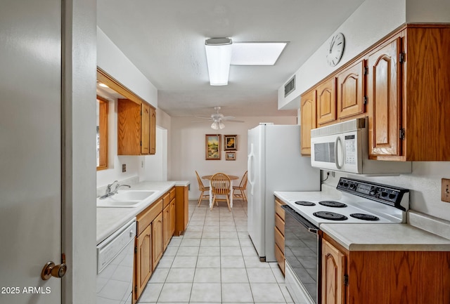 kitchen featuring a skylight, white appliances, ceiling fan, sink, and light tile patterned floors