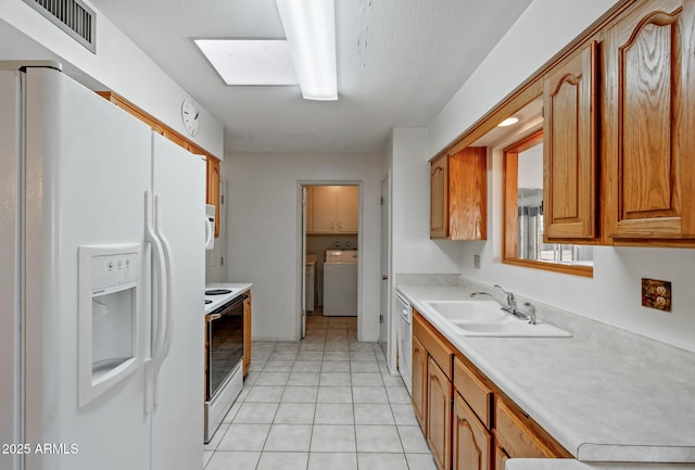 kitchen with white appliances, sink, light tile patterned floors, a textured ceiling, and separate washer and dryer