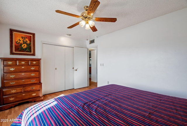 bedroom with ceiling fan, a closet, light hardwood / wood-style floors, and a textured ceiling