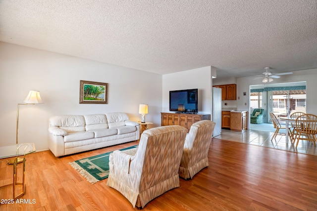 living room featuring light wood-type flooring, a textured ceiling, and ceiling fan